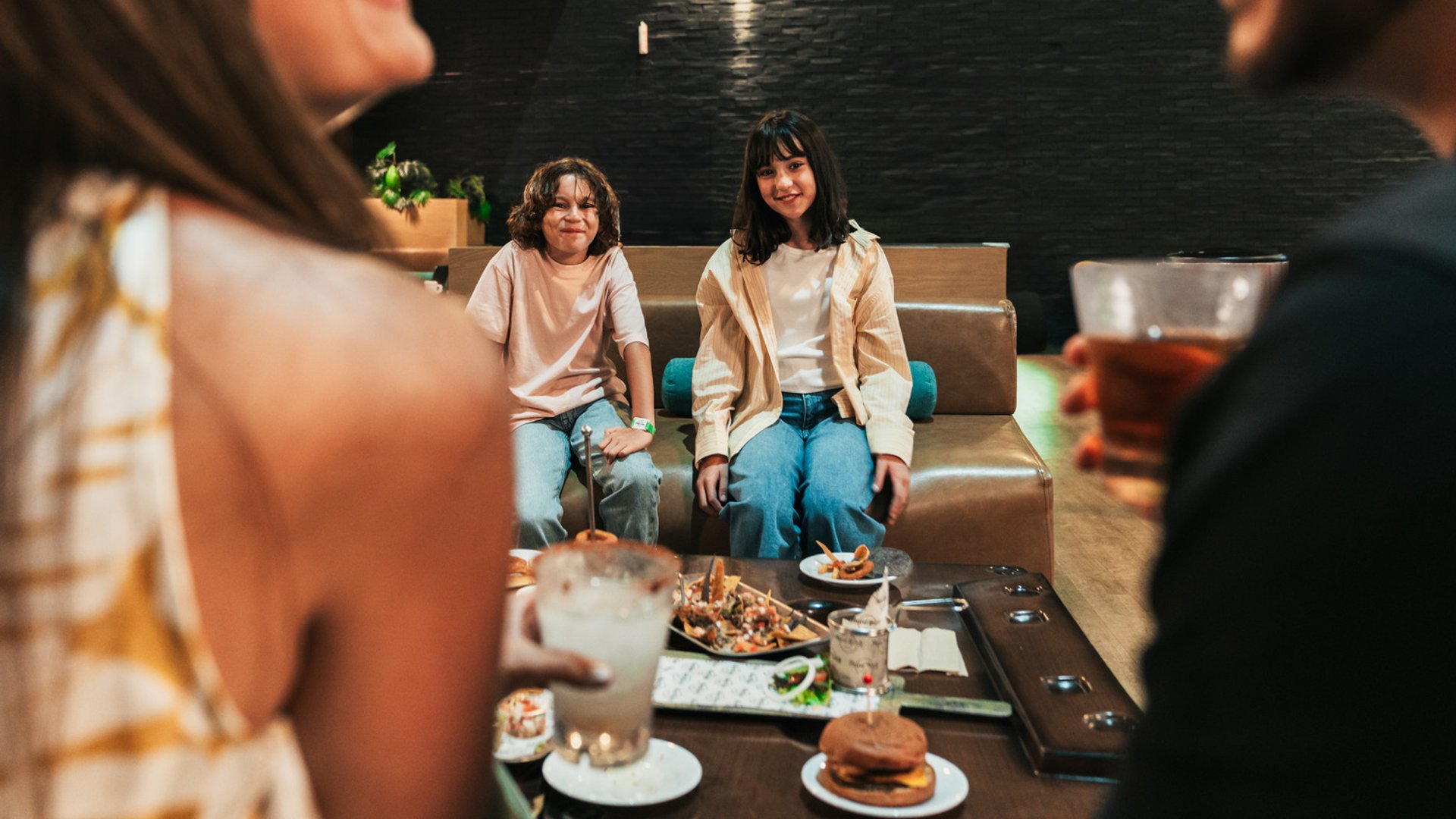 People enjoying drinks and food at a bowling alley lounge; focus on two seated individuals in the background.